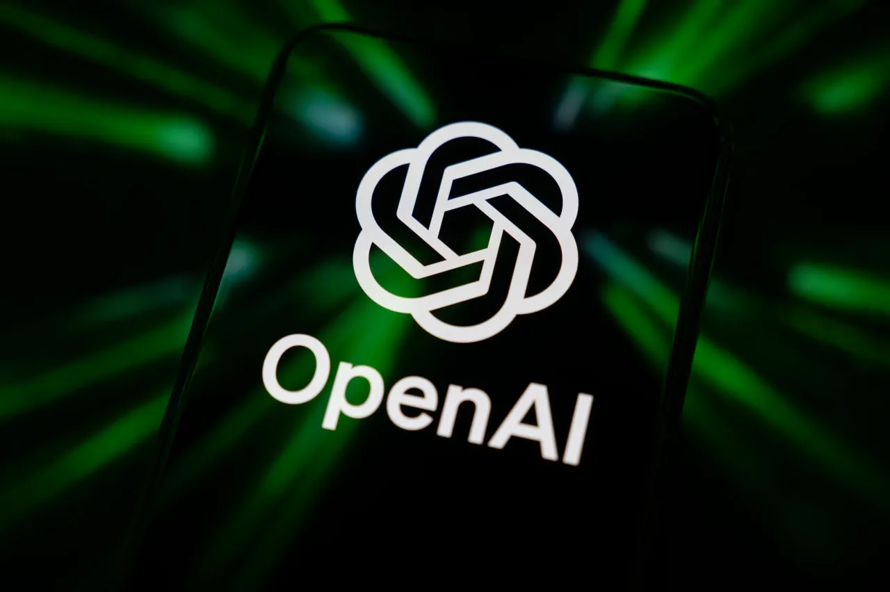 The OpenAI logo displays on a smartphone screen reflecting green beams. At DevDay 2025, OpenAI announced a slew of integrations with third-party apps. (Photo by Samuel Boivin/NurPhoto via Getty Images)