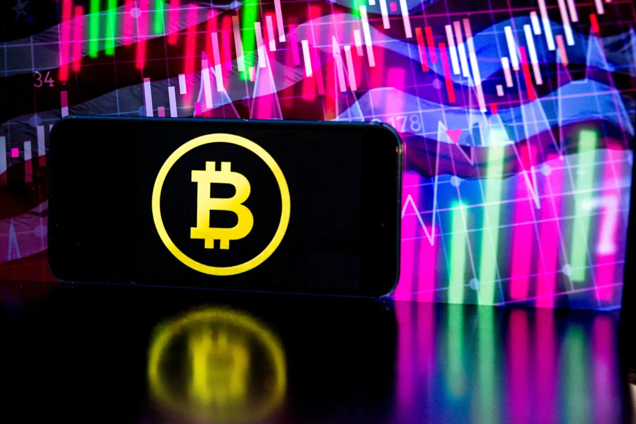 Bitcoin logo is shown on a mobile phone screen against a price chart in the background. (Photo by Dominika Zarzycka/NurPhoto via Getty Images)