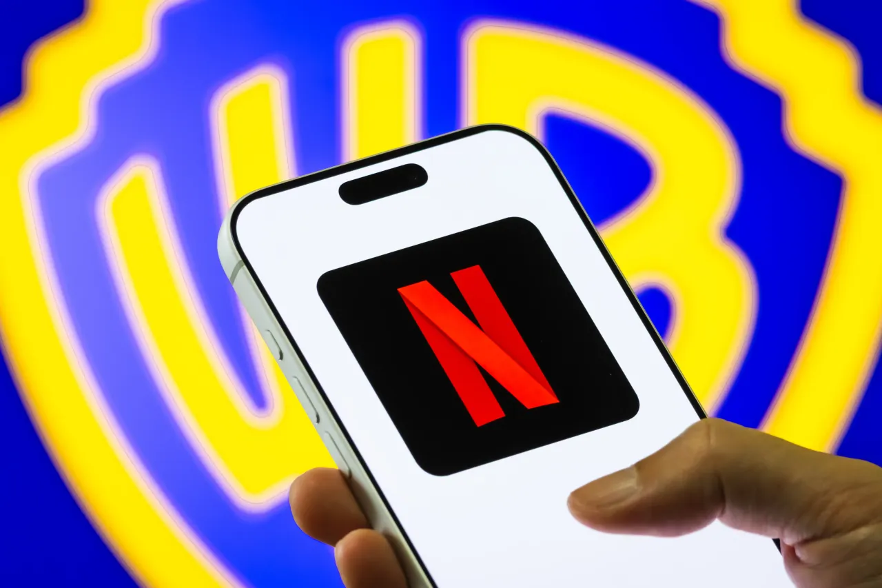 In this photo illustration, a smartphone displays the Netflix logo in front of a large blurred Warner Bros. Discovery emblem. (Photo illustration by Cheng Xin/Getty Images)