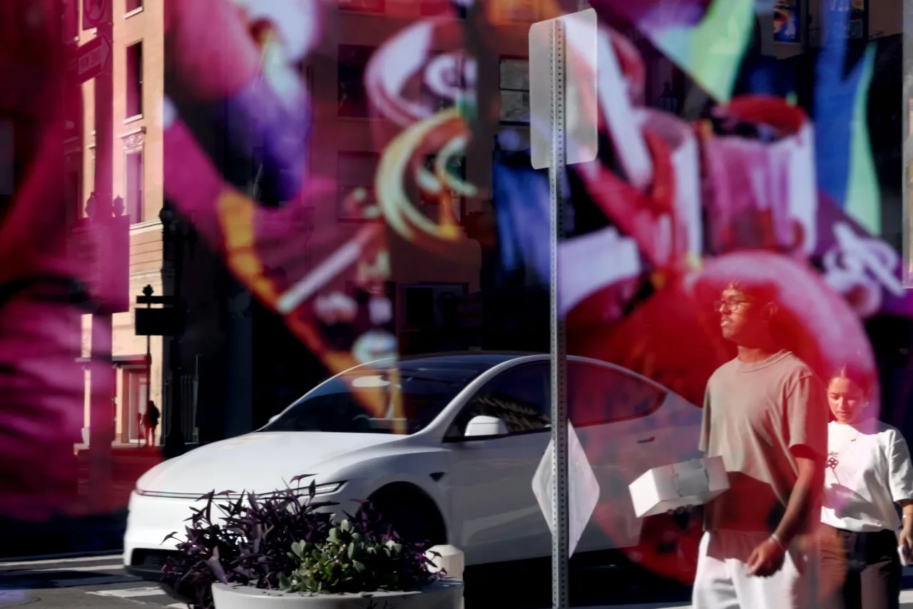 A Tesla car and pedestrians are caught in a storefront window while it drives down Broadway in downtown Los Angeles on January 8, 2026. (Genaro Molina/Los Angeles Times via Getty Images)