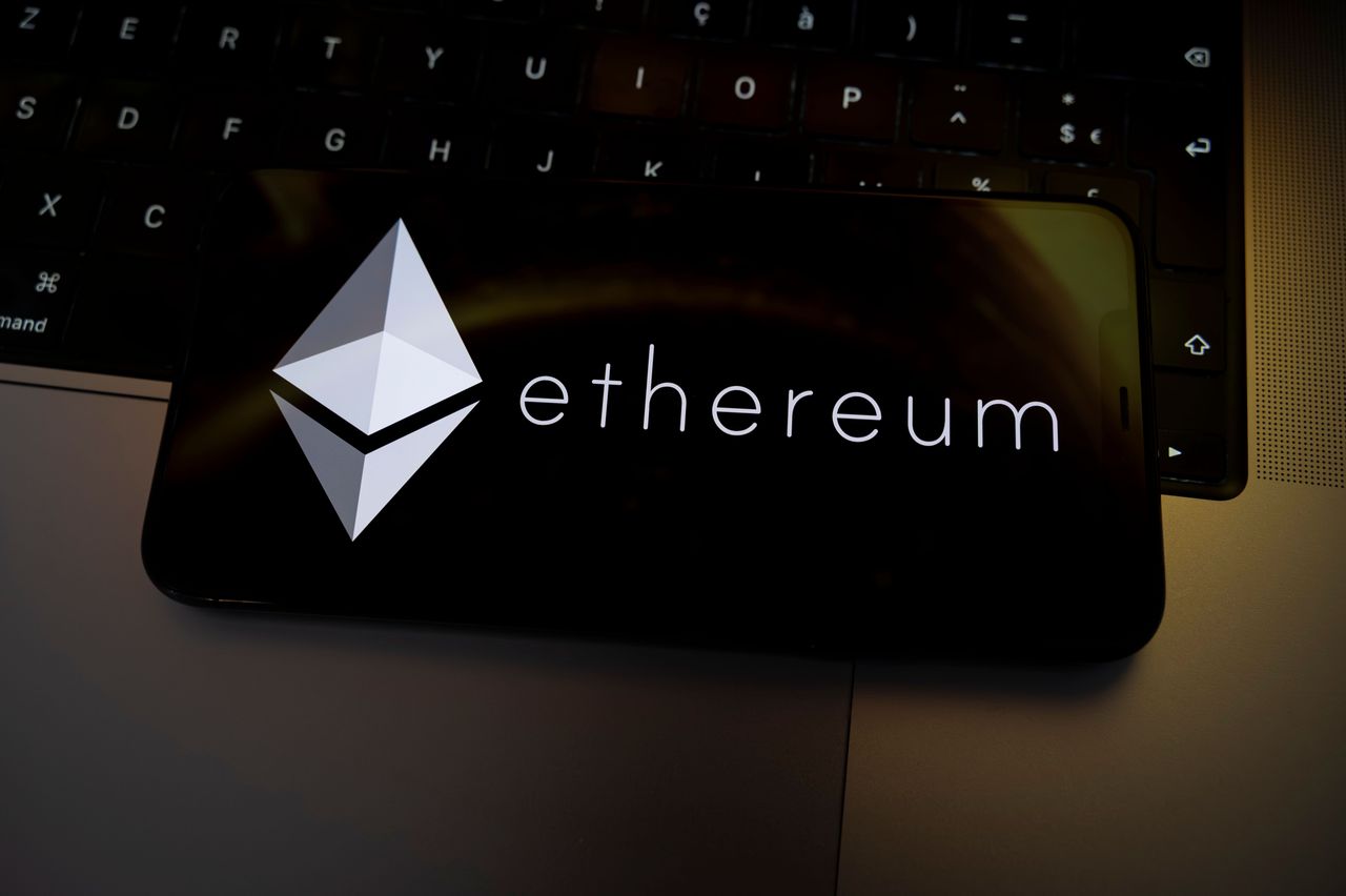 The Ethereum logo is displayed on the screen of a smartphone placed on a laptop keyboard illuminated by golden light. The global cryptocurrency market experiences a sharp decline, with Bitcoin falling below the key threshold of $75,000, dragging major altcoins down with it in Creteil, France, on February 3, 2026. (Photo by Samuel Boivin/NurPhoto via Getty Images)