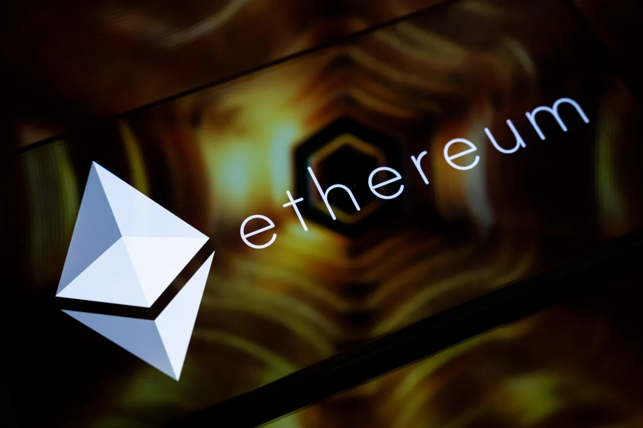 The Ethereum logo is displayed on the screen of a smartphone placed on a reflective surface onto which a golden illustration is projected. (Photo by Samuel Boivin/NurPhoto via Getty Images)