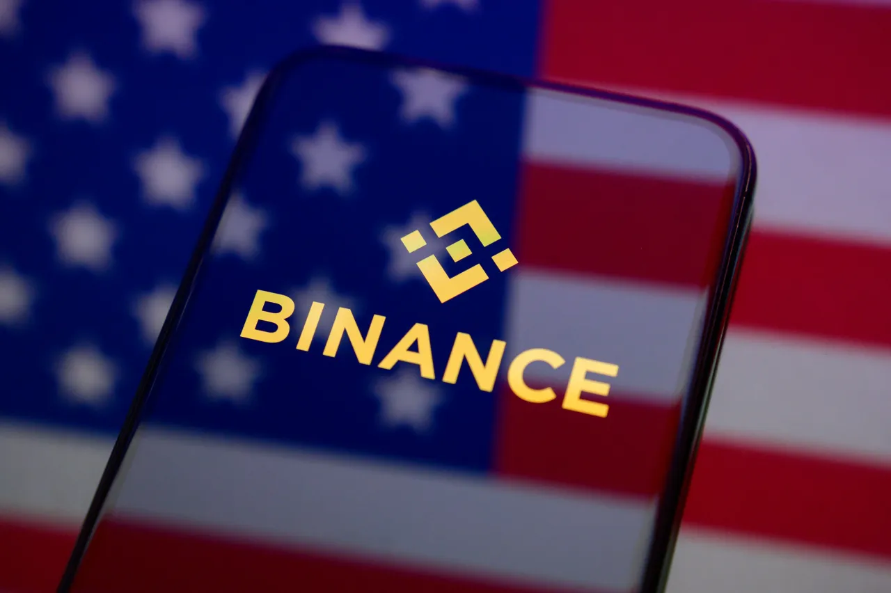 The Binance logo appears on a smartphone screen placed on a reflective surface onto which a US flag is projected. (Photo Illustration by Samuel Boivin/NurPhoto via Getty Images)