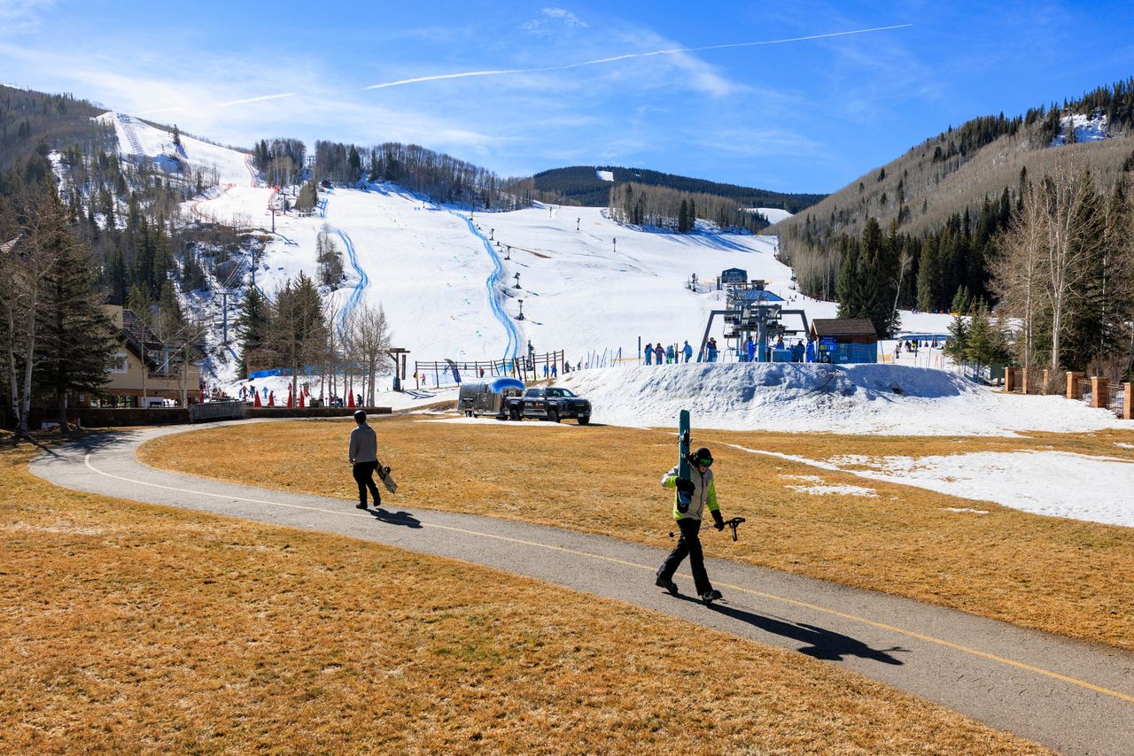A skier and snowboarder walk through a grassy field to the chairlift at Vail Ski Resort in Colorado.