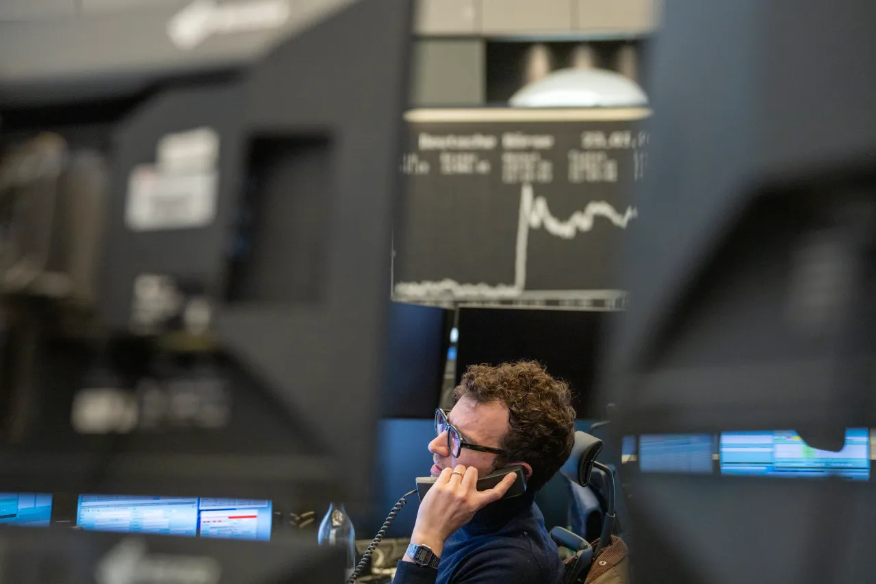 A trader sits at his desk and the daily performance of the German share index (Dax) can be seen in the background on the large display board above the trading floor. Photo: Andreas Arnold/dpa (Photo by Andreas Arnold/picture alliance via Getty Images)