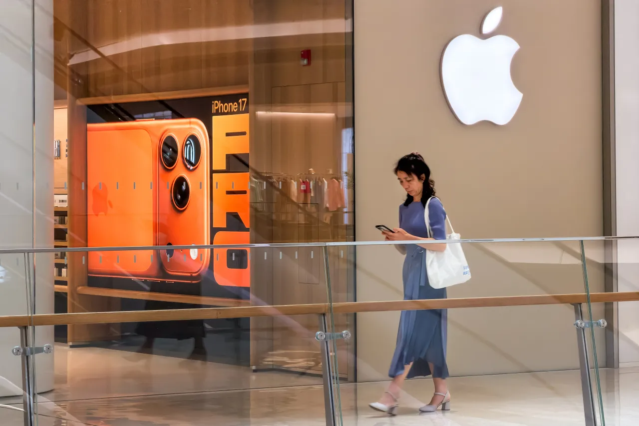 A pedestrian looks at a smartphone while walking past an Apple Store featuring an iPhone 17 Pro advertisement inside a shopping mall in Shenzhen, China. (Photo by Cheng Xin/Getty Images)