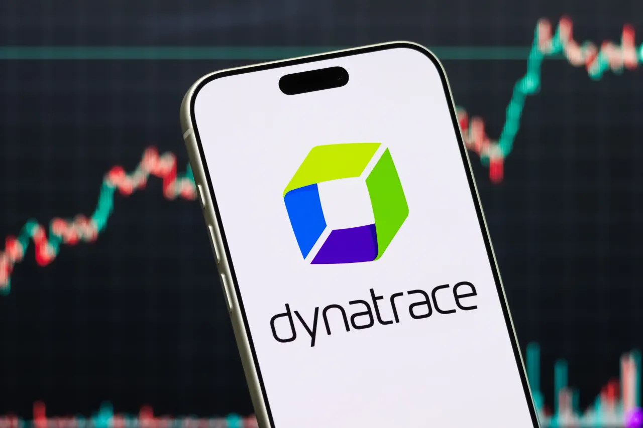 A smartphone displays the logo of Dynatrace Inc. (DT) in front of a screen showing the company's stock market chart. (Photo illustration by Cheng Xin/Getty Images)