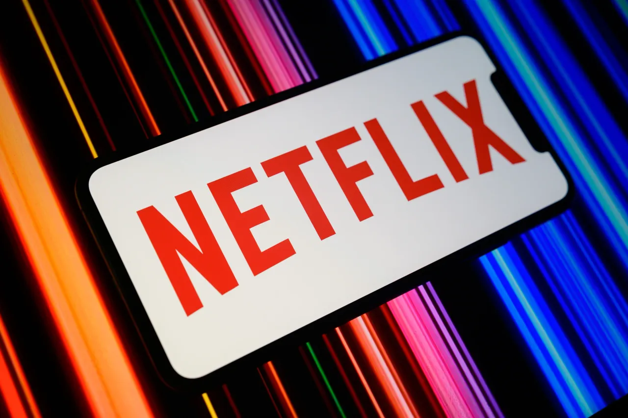 The Netflix logo is displayed on a smartphone screen with a promotional image featuring a color gradient in the background. (Photo by Samuel Boivin/NurPhoto via Getty Images)