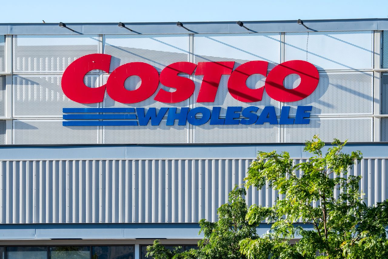 The upper exterior corporate logo of a Costco Wholesale warehouse is mounted on the building facade in United States.