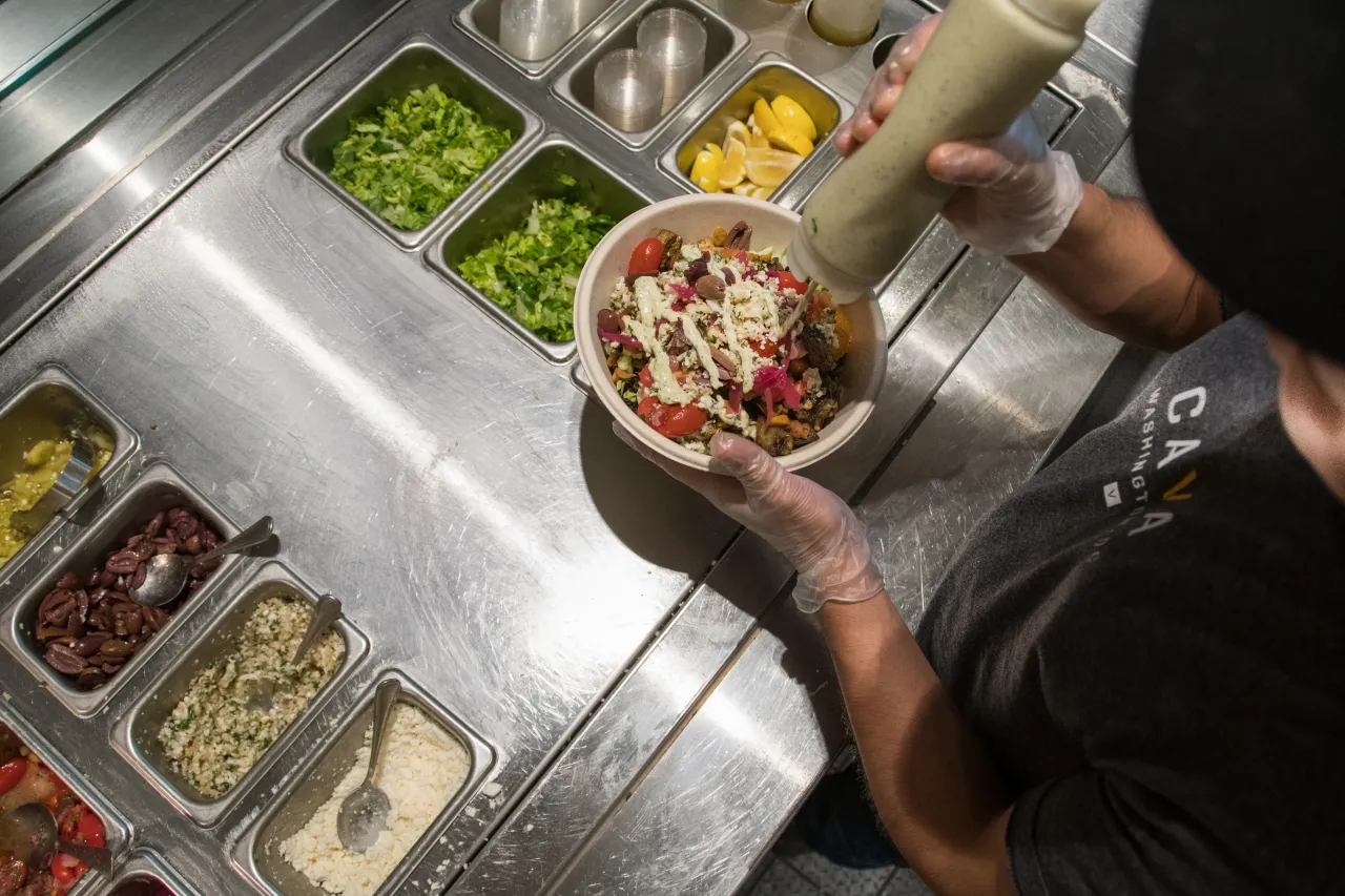 Toppings being put on a bowl at Cava.