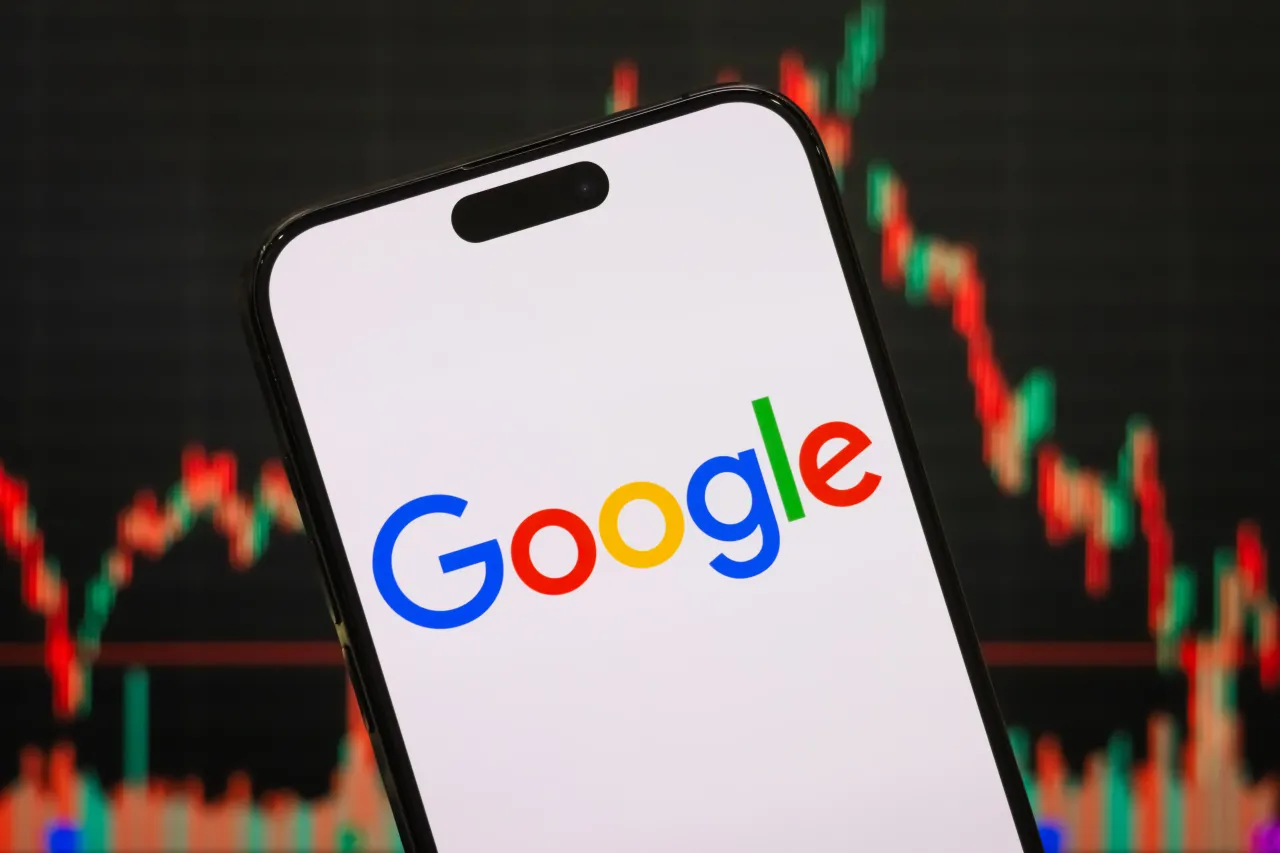 The logo of Google is displayed on a smartphone screen, with the company’s stock market performance and candlestick chart visible in the background. (Photo illustration by Cheng Xin/Getty Images)