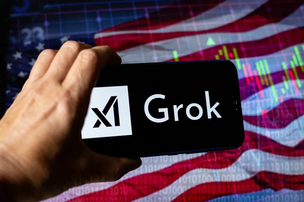 In this photo illustration, the xAI Grok logo is seen displayed on a mobile phone against the USA national flag and stock graph in the background. 
