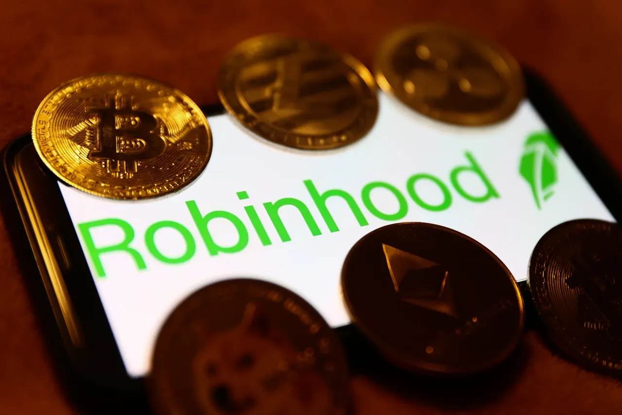 Robinhood logo displayed on a phone screen and representation of cryptocurrencies.
