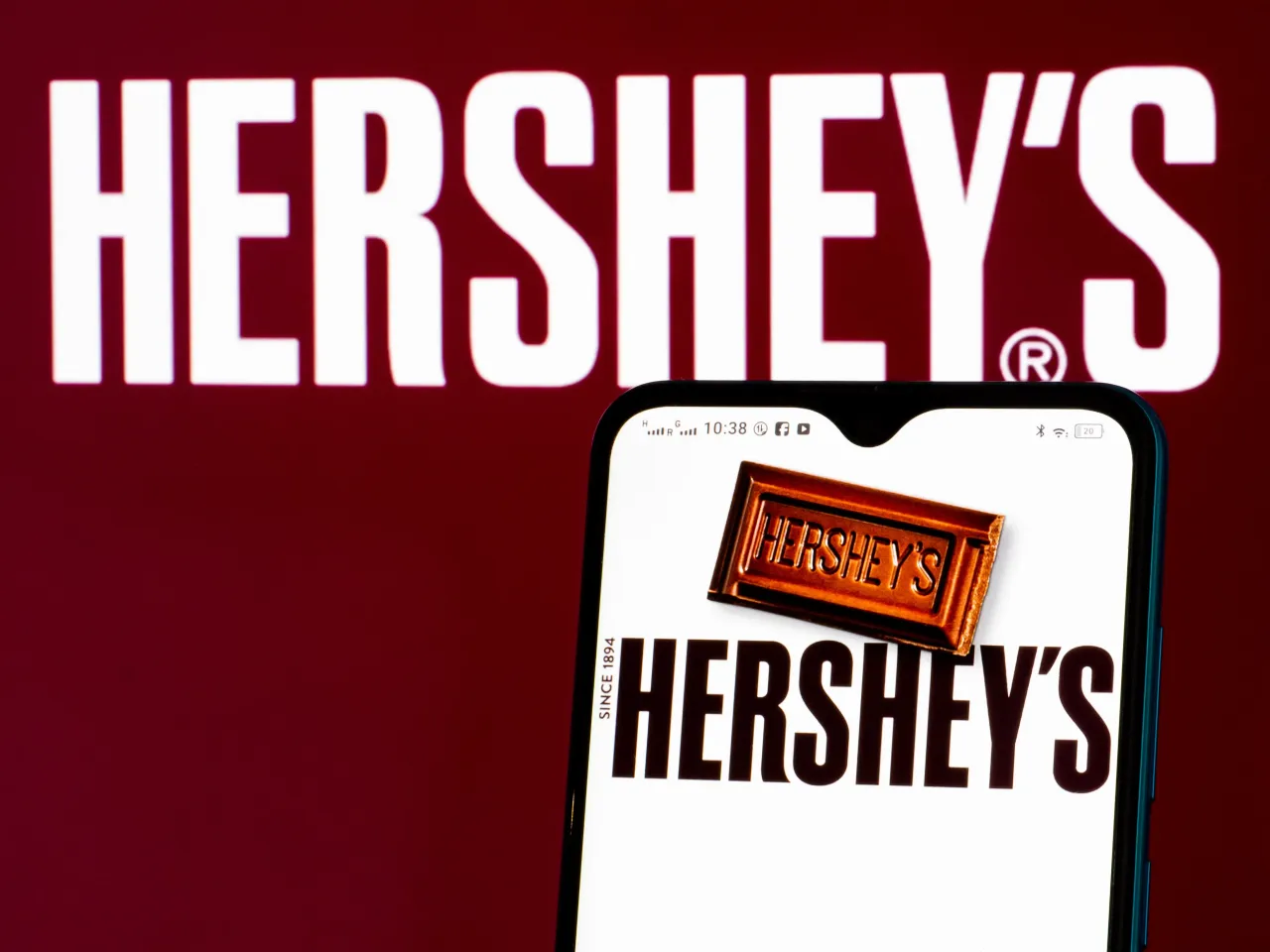 In this photo illustration, The Hershey Company logo seen displayed on a smartphone and in the background.