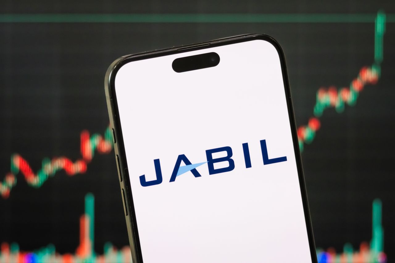 The logo of Jabil Inc. is displayed on a smartphone screen, with the company's stock market chart in the background. (Photo Illustration by Cheng Xin/Getty Images)