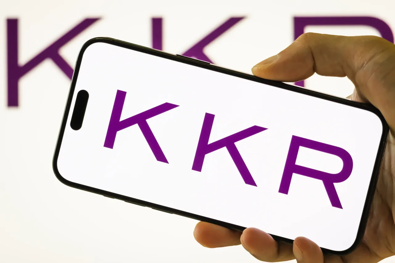 In this photo illustration, a person holds a smartphone displaying the logo of KKR & Co. Inc. 