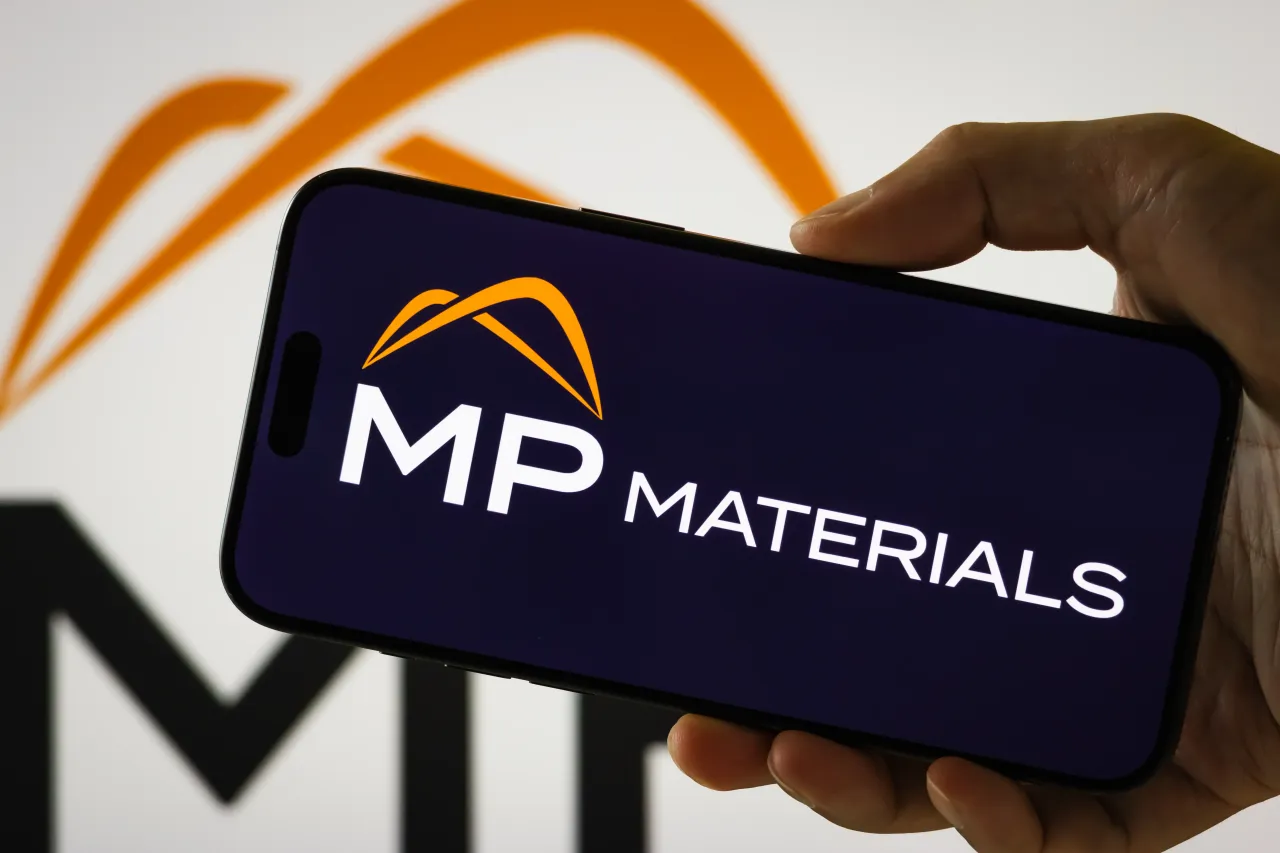 In this photo illustration, a person holds a smartphone displaying the logo of MP Materials Corp. (NYSE: MP).