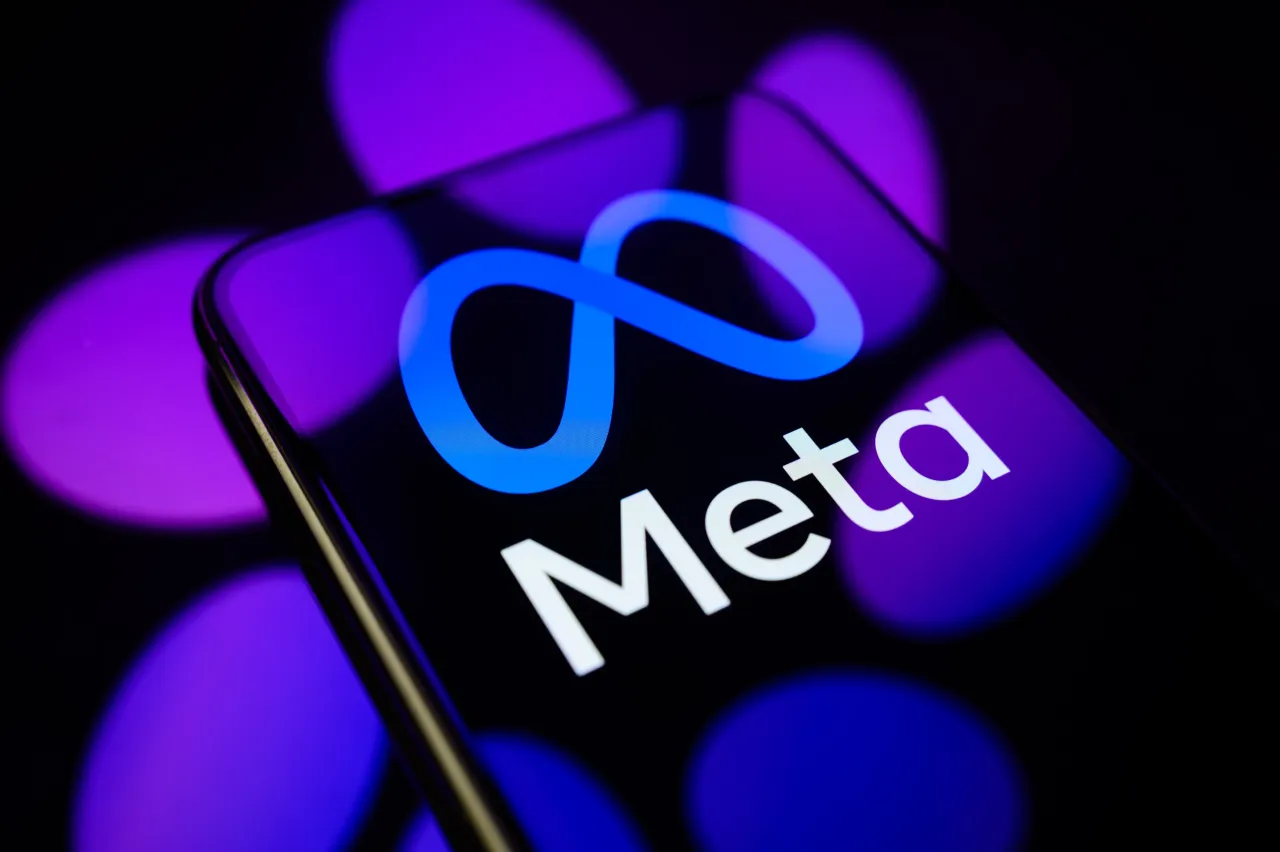 The Meta logo is displayed on a smartphone screen placed on a reflective surface onto which the Meta AI logo is projected. (Photo by Samuel Boivin/NurPhoto via Getty Images)