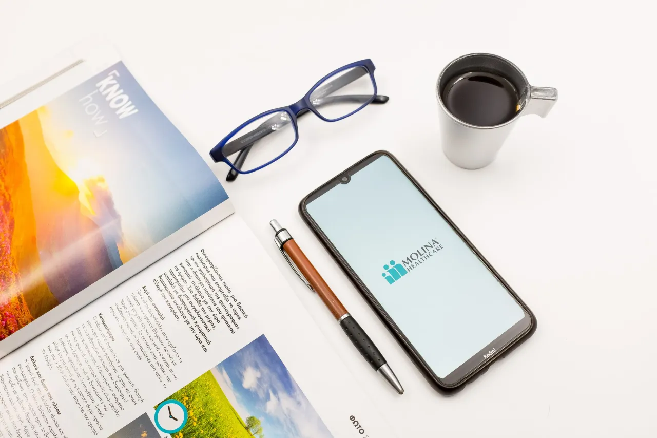 In this photo illustration a Molina Healthcare logo seen displayed on a smartphone screen on a desk next to a cafe, a pen, glasses and a magazine in Athens, Greece on June 5, 2022.