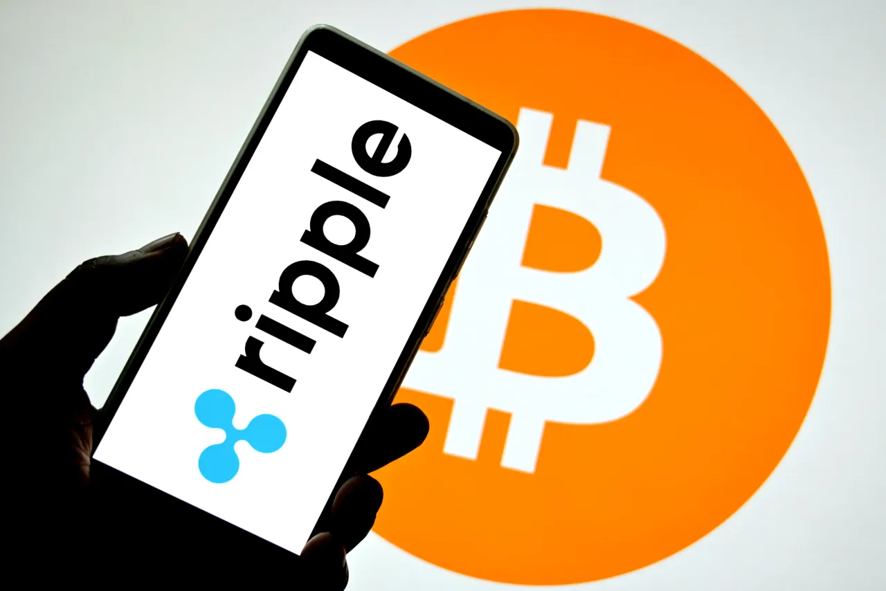 In this photo illustration, a Ripple logo is seen displayed on a smartphone with a Bitcoin logo in the background.