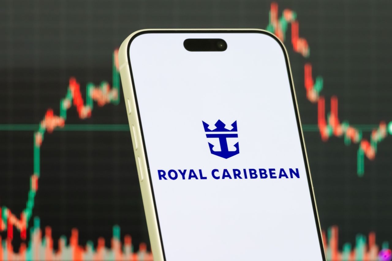A smartphone displays the logo of Royal Caribbean Group in front of a screen showing the company's stock market chart. (Photo illustration by Cheng Xin/Getty Images)