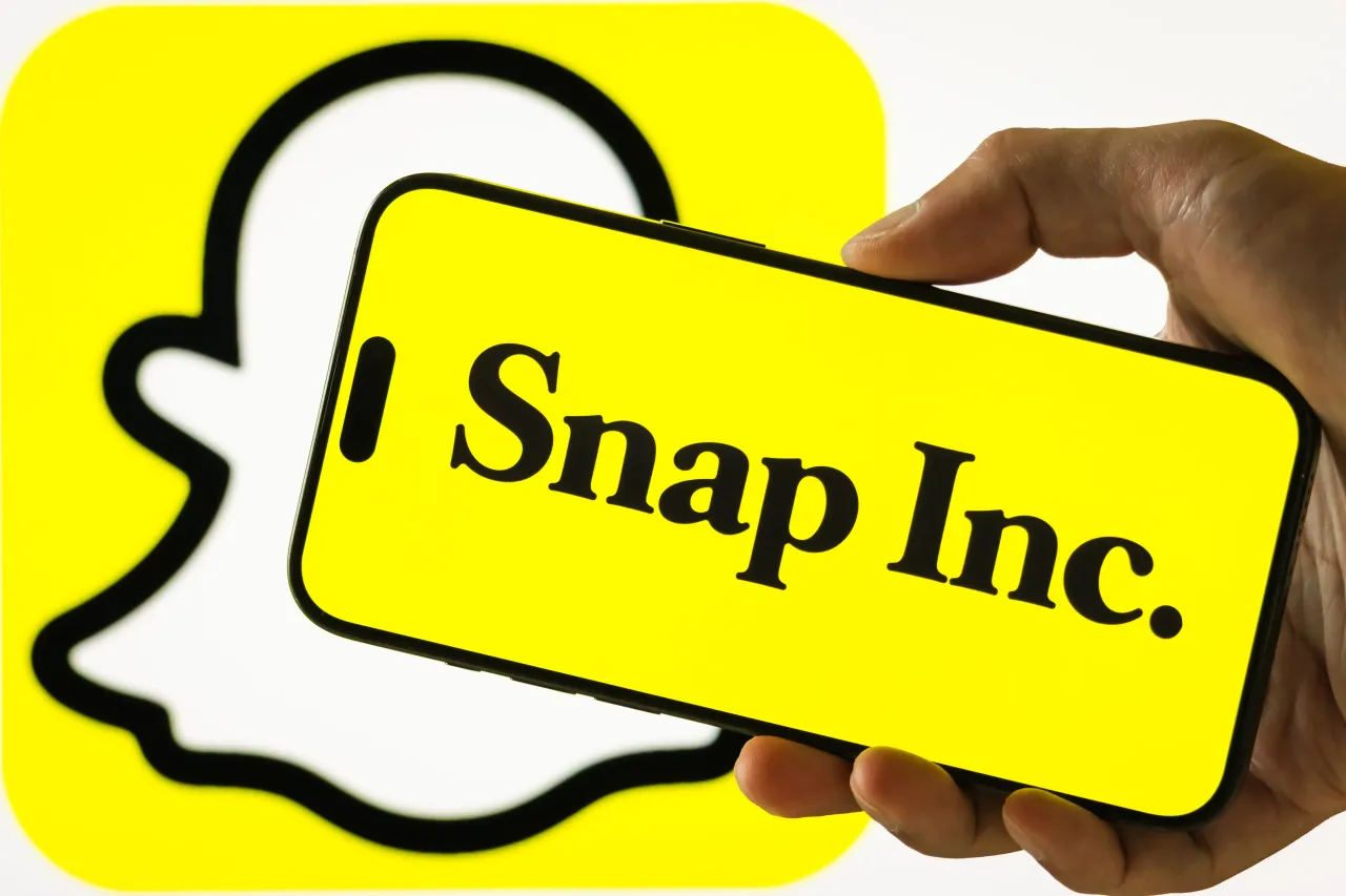 In this photo illustration, a person holds a smartphone displaying the logo of Snap Inc. (NYSE: SNAP), the parent company of Snapchat, on July 31, 2025, in Chongqing, China. (Photo illustration by Cheng Xin/Getty Images)