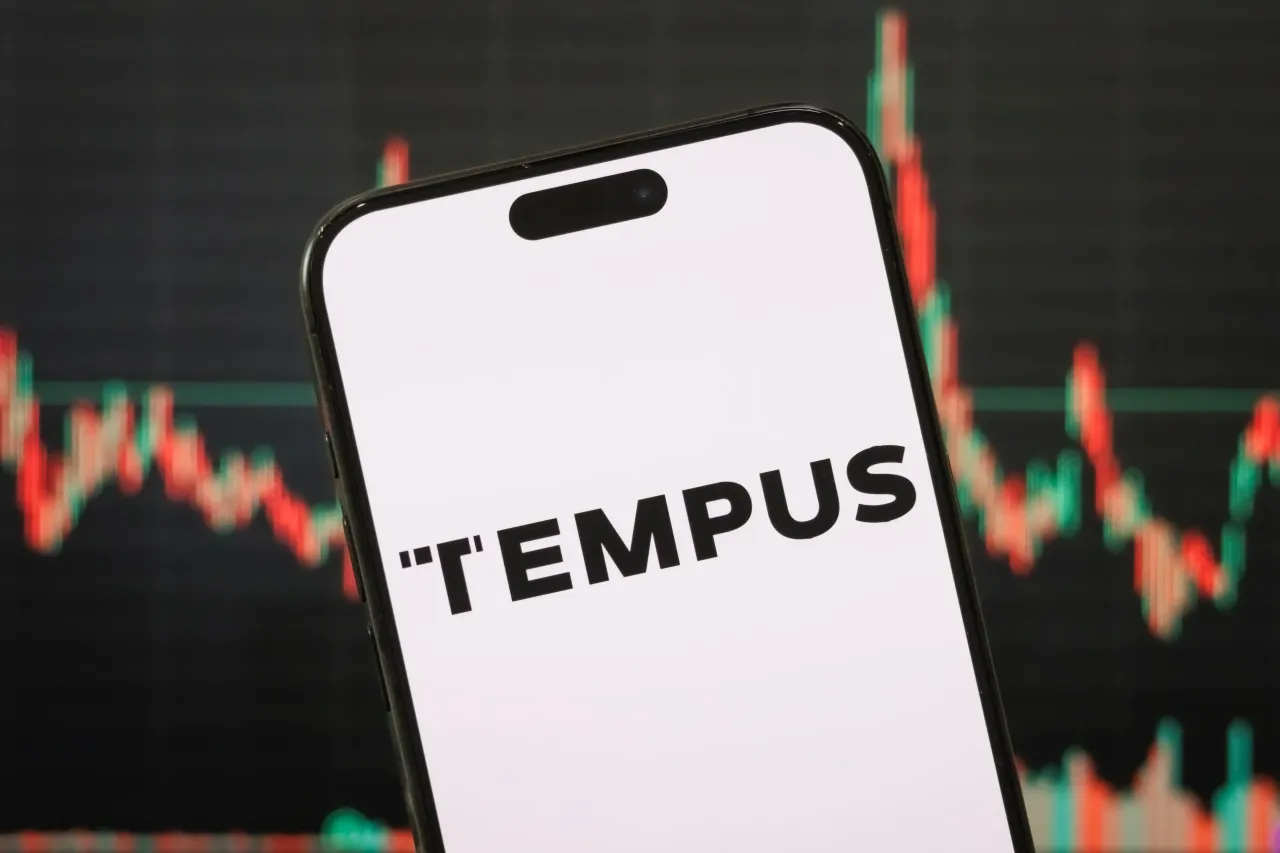 The logo of Tempus AI is displayed on a smartphone screen, with a stock market chart in the background. (Photo illustration by Cheng Xin/Getty Images)