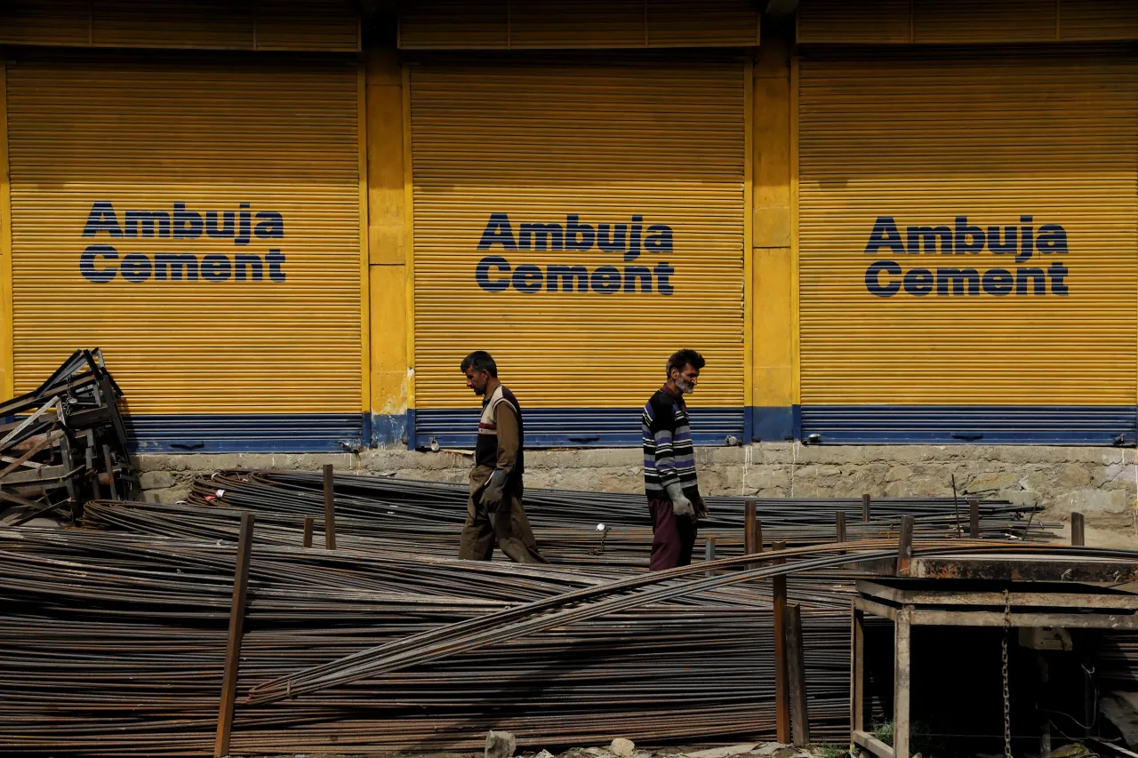 Laborers carry iron rods as Ambuja Cement advertisement is seen on the closed shutters near a construction selling items area in Sopore, District Baramulla, Jammu and Kashmir, India on 14 April 2022. (Photo by Nasir Kachroo/NurPhoto via Getty Images)