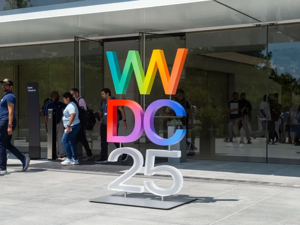 Attendees of the Apple developer conference WWDC walk in front of a logo of the event next to the company's headquarters. (Photo by Andrej Sokolow/picture alliance via Getty Images)