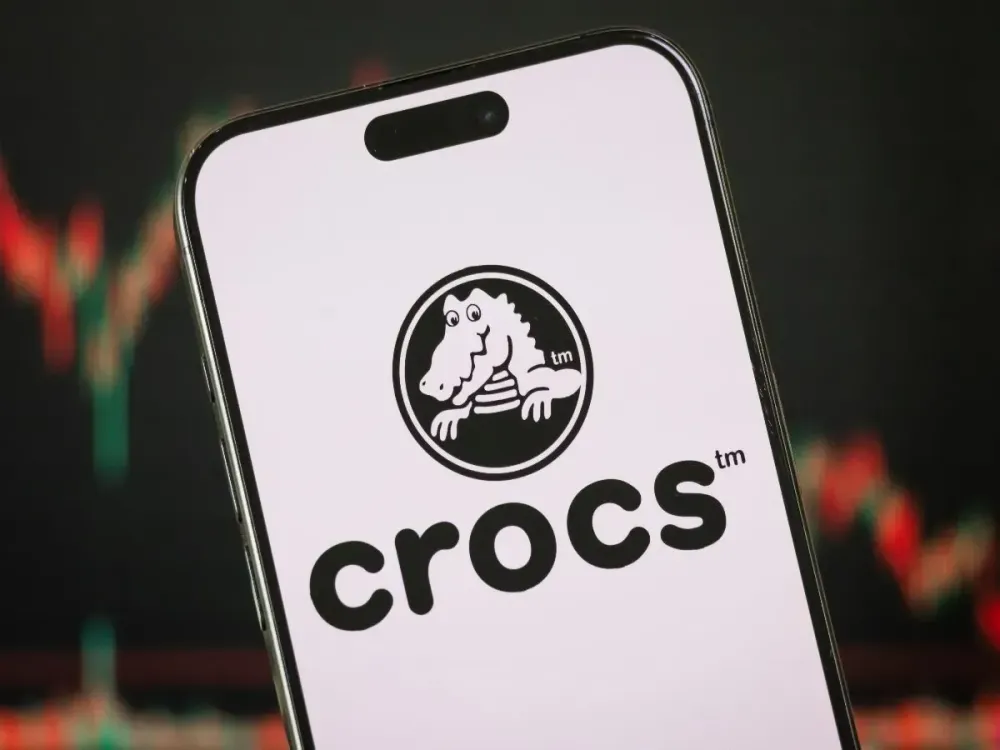  In this photo illustration, the Crocs logo is displayed on a smartphone screen in front of a stock chart showcasing Crocs' financial performance on Feb. 10, 2025, in Chongqing, China. (Photo illustration by Cheng Xin/Getty Images)
