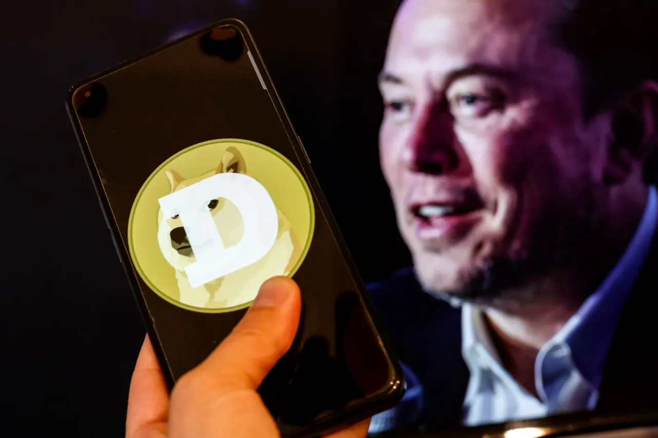 The Dogecoin logo is seen displayed on a smartphone with a computer screen displaying a portrait of Elon Musk in the background. (Photo Illustration by Dominika Zarzycka/SOPA Images/LightRocket via Getty Images)