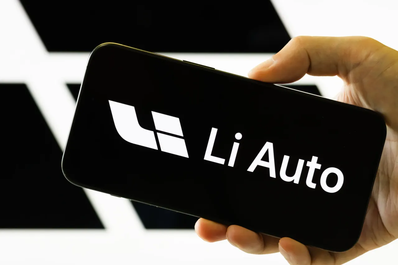 In this photo illustration, a person holds a smartphone displaying the logo of Li Auto Inc, with the company's branding visible in the background on August 26, 2025. (Photo by Cheng Xin/Getty Images)