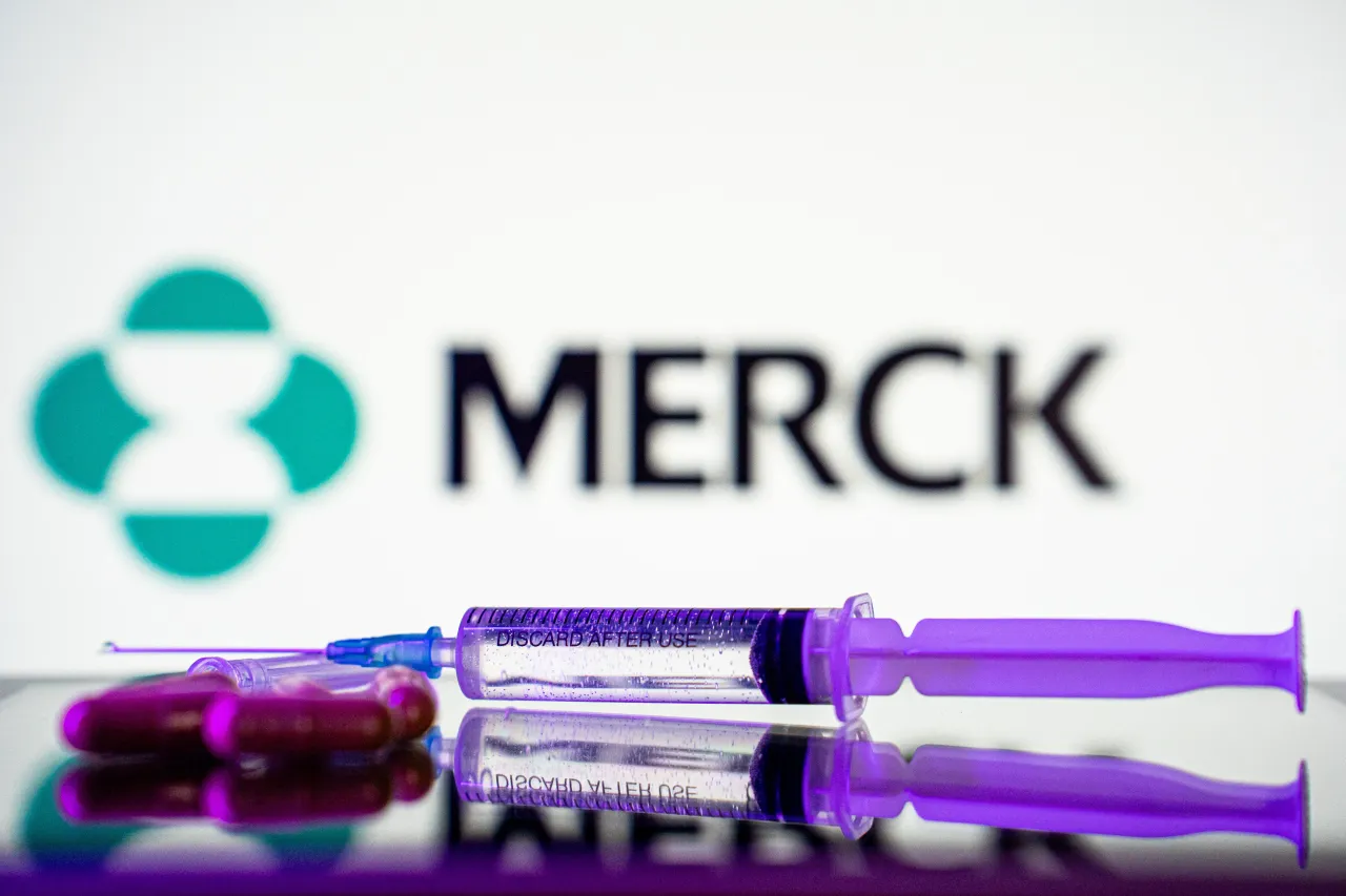 A syringe and some pills are in front of the logo of Merck pharmaceutical company. (Photo by Nikos Pekiaridis/NurPhoto via Getty Images)