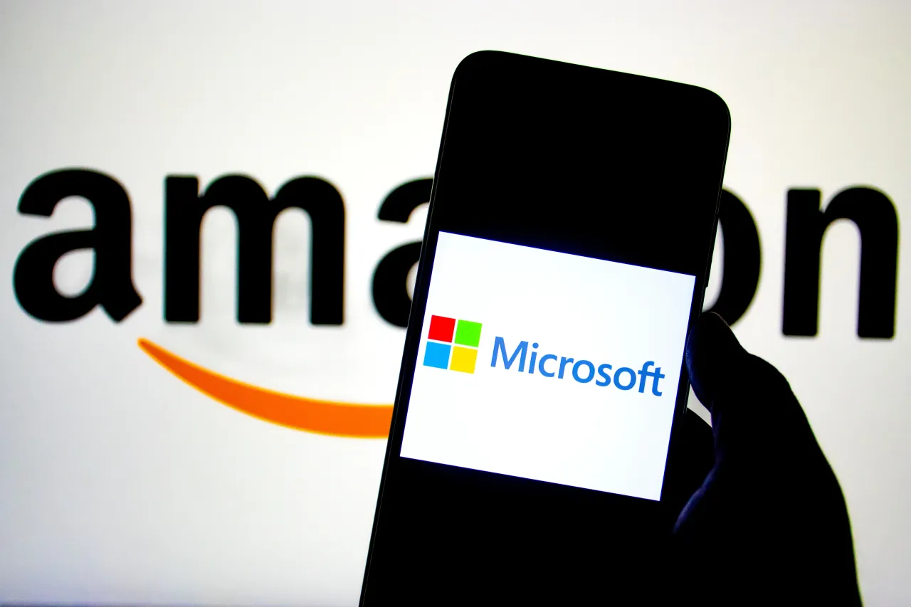 In this photo illustration, a Microsoft logo seen displayed on a smartphone with an Amazon Logo in the background