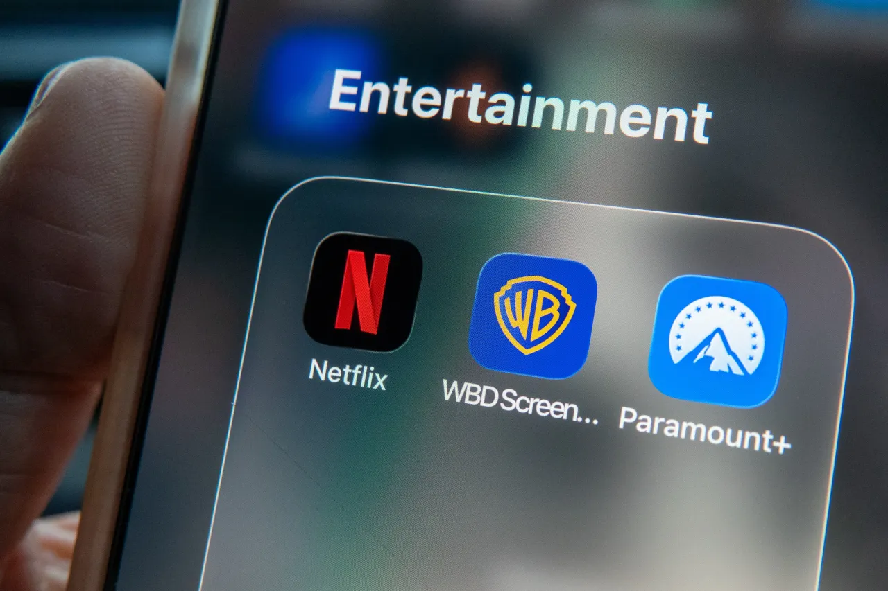 In this photo illustration a man holds a iPhone, that shows Netflix, Warner Bros and Paramount streaming apps on his phone screen