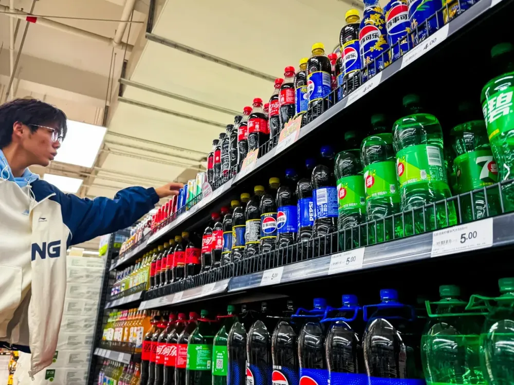 A young man browses the soda aisle, selecting from popular brands such as Pepsi, Coca-Cola, and 7Up, at a supermarket on October 20, 2024 in Chongqing, China. (Photo by Cheng Xin/Getty Images)