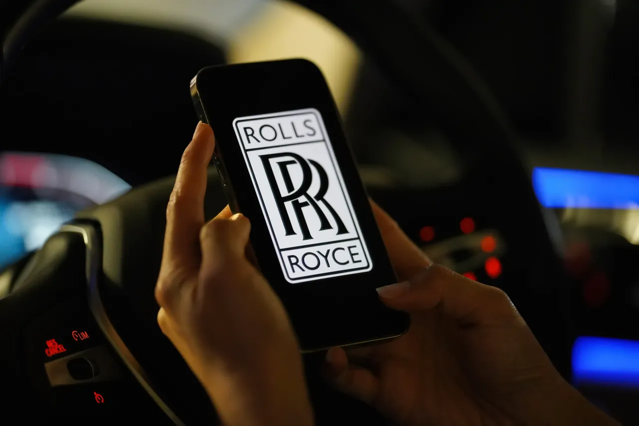In this photo illustration, the logo of Rolls-Royce is seen on a smartphone screen with a steering wheel in the background. (Photo Illustration by Serene Lee/SOPA Images/LightRocket via Getty Images)