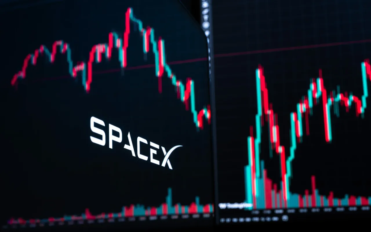 The logo of the U.S. aerospace, telecommunications, and AI company SpaceX is visible on a MacBook screen in front of a candlestick chart of SpaceX stock on TradingView. Photo: Silas Stein/dpa (Photo by Silas Stein/picture alliance via Getty Images)