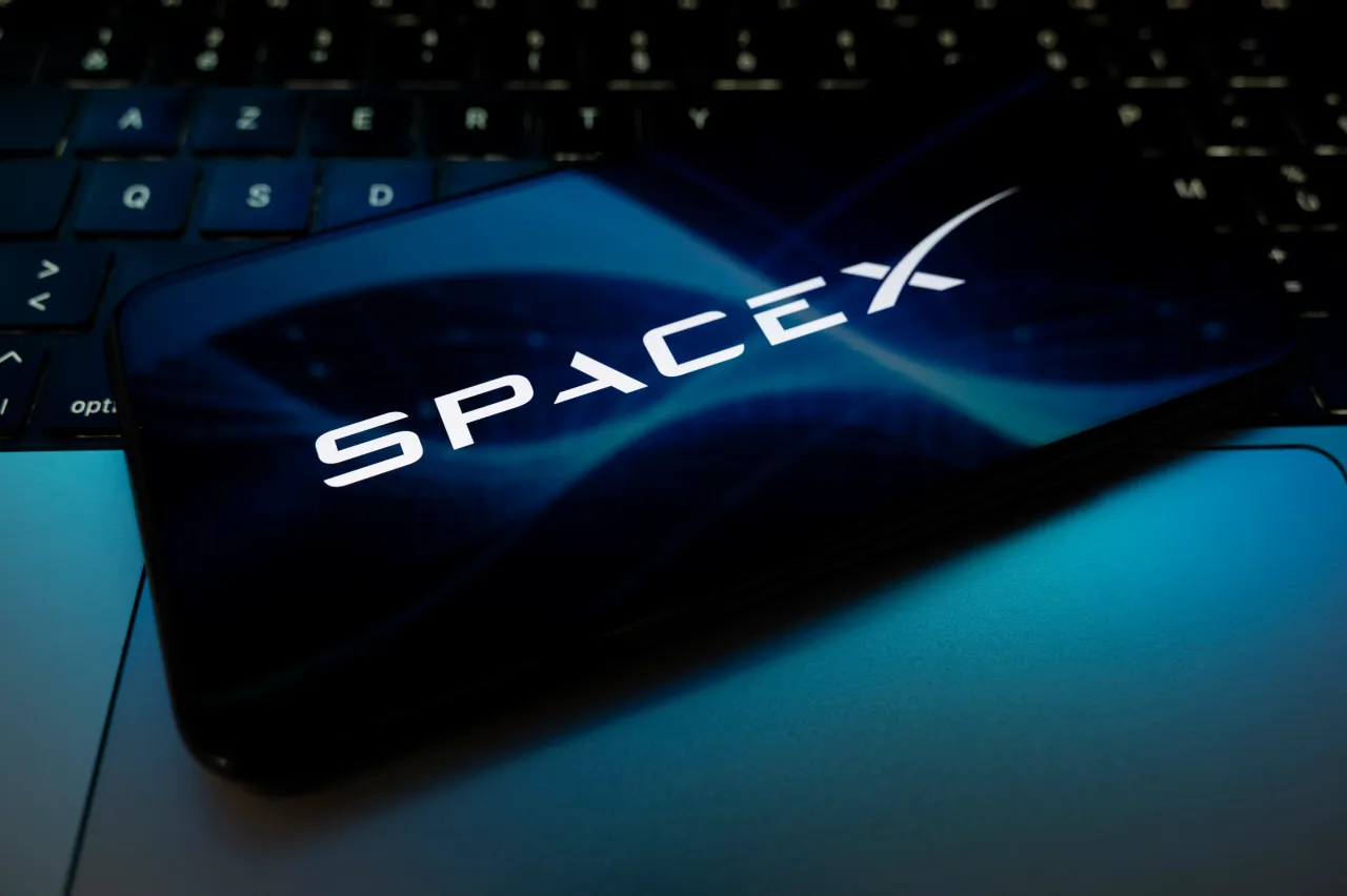The SpaceX logo appears on a smartphone screen placed on a laptop keyboard illuminated by blue light. (Photo by Samuel Boivin/NurPhoto via Getty Images)