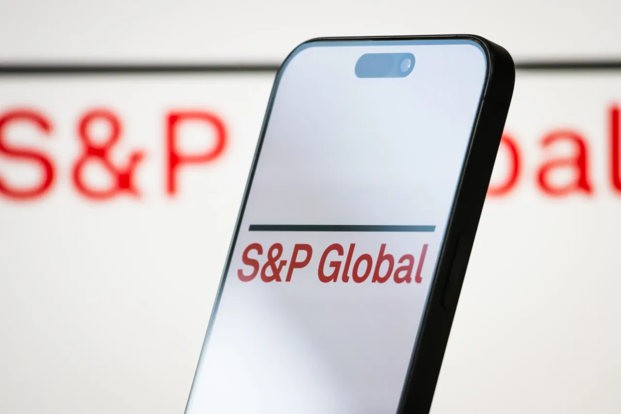 In this photo illustration, the logo of S&P Global Inc. is displayed on a smartphone screen, with the company's red branding and name visible in the background, on April 23, 2025. (Photo illustration by Cheng Xin/Getty Images)