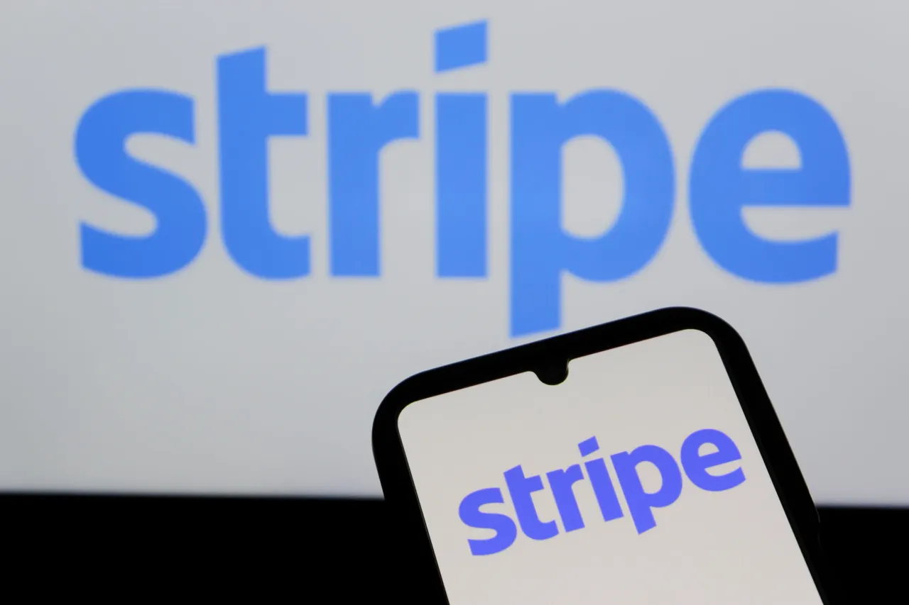 In this photo illustration, the Stripe logo is displayed on a smartphone with Stripe Payment Processing Website in the background