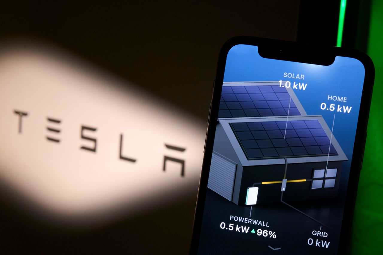 The Tesla app Power Flow screen is seen displayed on a smartphone, showing live energy distribution between solar panels generating 1.0 kW, the home consuming 0.5 kW and a Powerwall battery at 96 percent supplying 0.5 kW, with the Tesla logo visible blurred in the background, in this illustration photo taken on July 31, 2026. (Photo by Matteo Della Torre/NurPhoto via Getty Images)