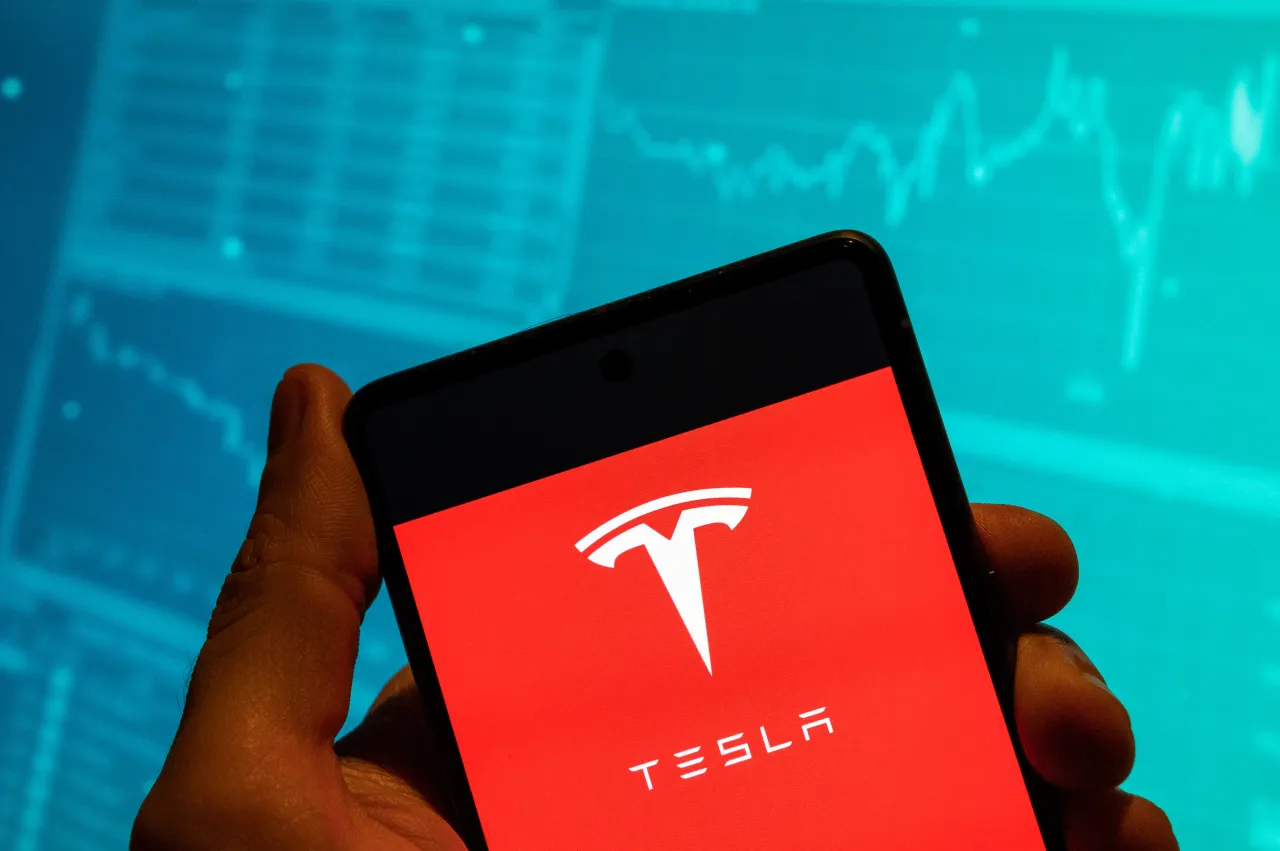 In this photo illustration, Tesla logo is seen displayed on a smartphone with an economic stock exchange index graph in the background. (Photo Illustration by Budrul Chukrut/SOPA Images/LightRocket via Getty Images)
