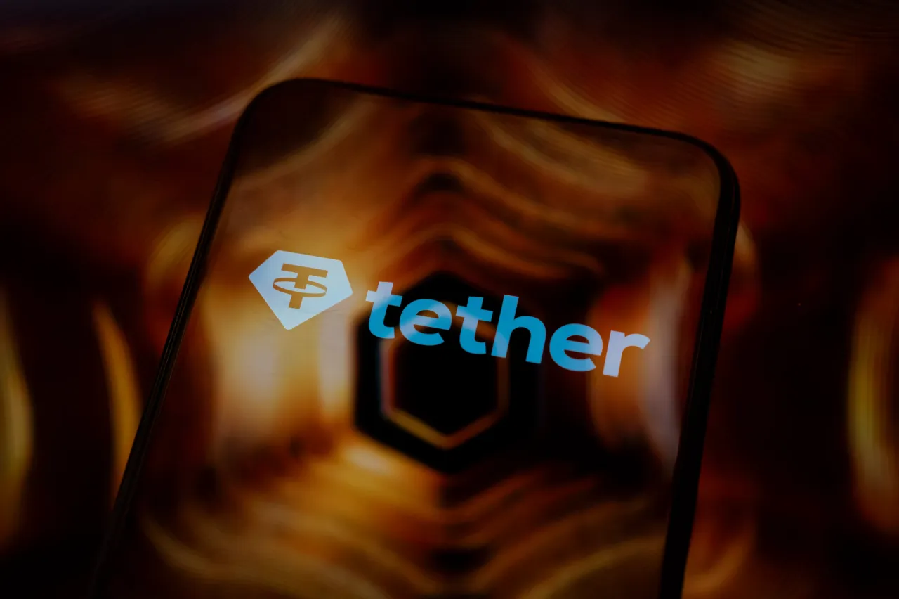 The Tether logo is displayed on the screen of a smartphone placed on a reflective surface onto which a golden illustration is projected. (Photo by Samuel Boivin/NurPhoto via Getty Images)