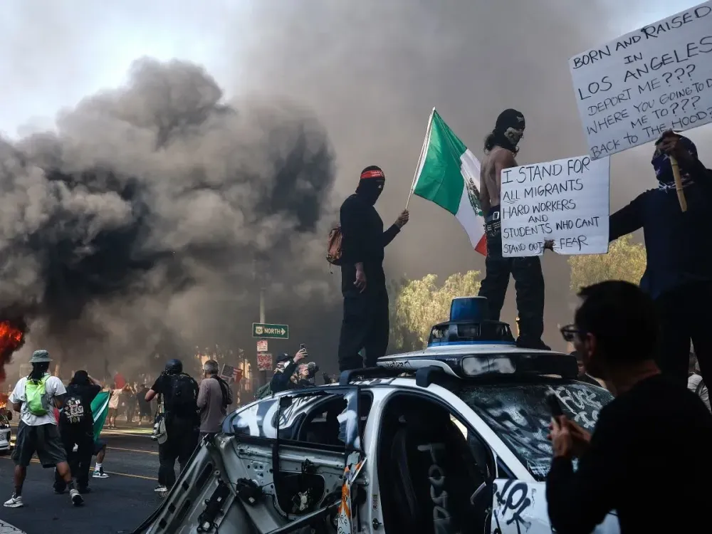 Protestors stand atop a vandalized Waymo car during immigration raid protests on June 08, 2025 in Los Angeles, California