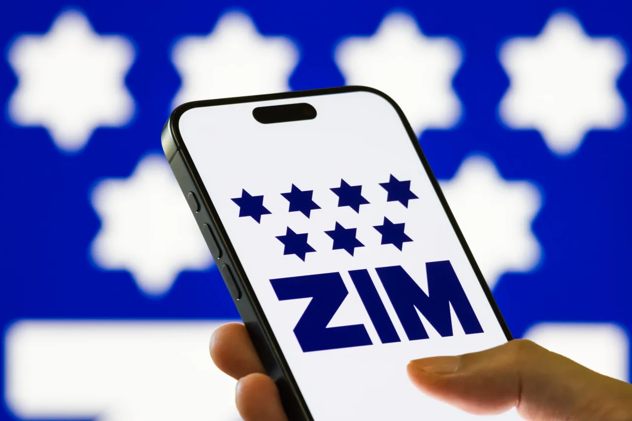 In this photo illustration, a person holds a smartphone displaying the logo of ZIM Integrated Shipping Services Ltd. (NYSE: ZIM) on August 18, 2025. (Photo illustration by Cheng Xin/Getty Images)