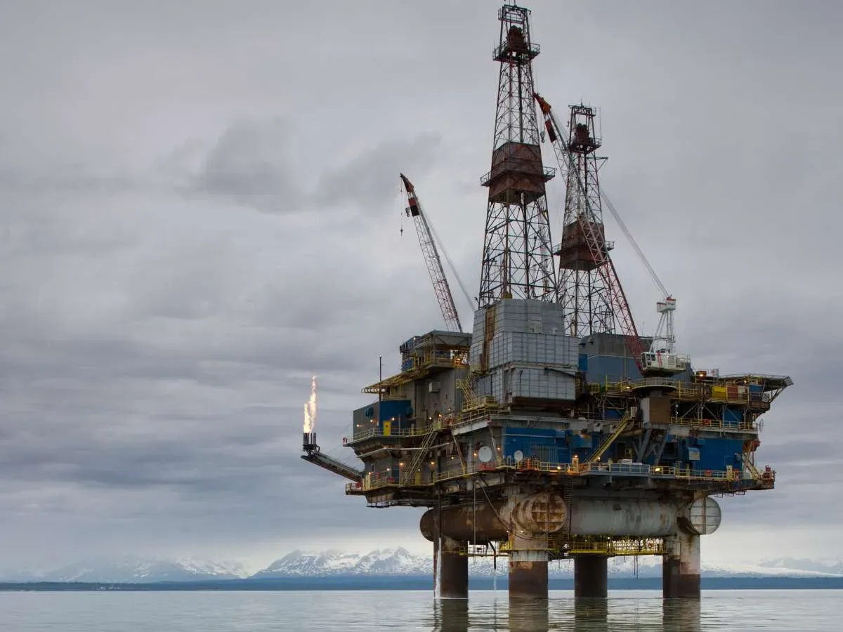 Offshore oil drilling rig in Cook Inlet with distant Alaska Range peaks on summer evening.